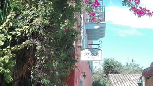 A narrow street with a hotel named "Byron Hotel" on the right, surrounded by lush greenery and vibrant pink bougainvillea flowers. - Byron Hotel (Nafplio)
