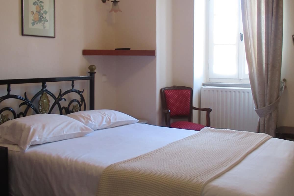 A bed with white linens, a red chair, a wall-mounted light fixture, and a window with curtains.