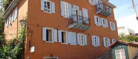 Un edificio de varios pisos con fachada roja, contraventanas blancas y balcones.