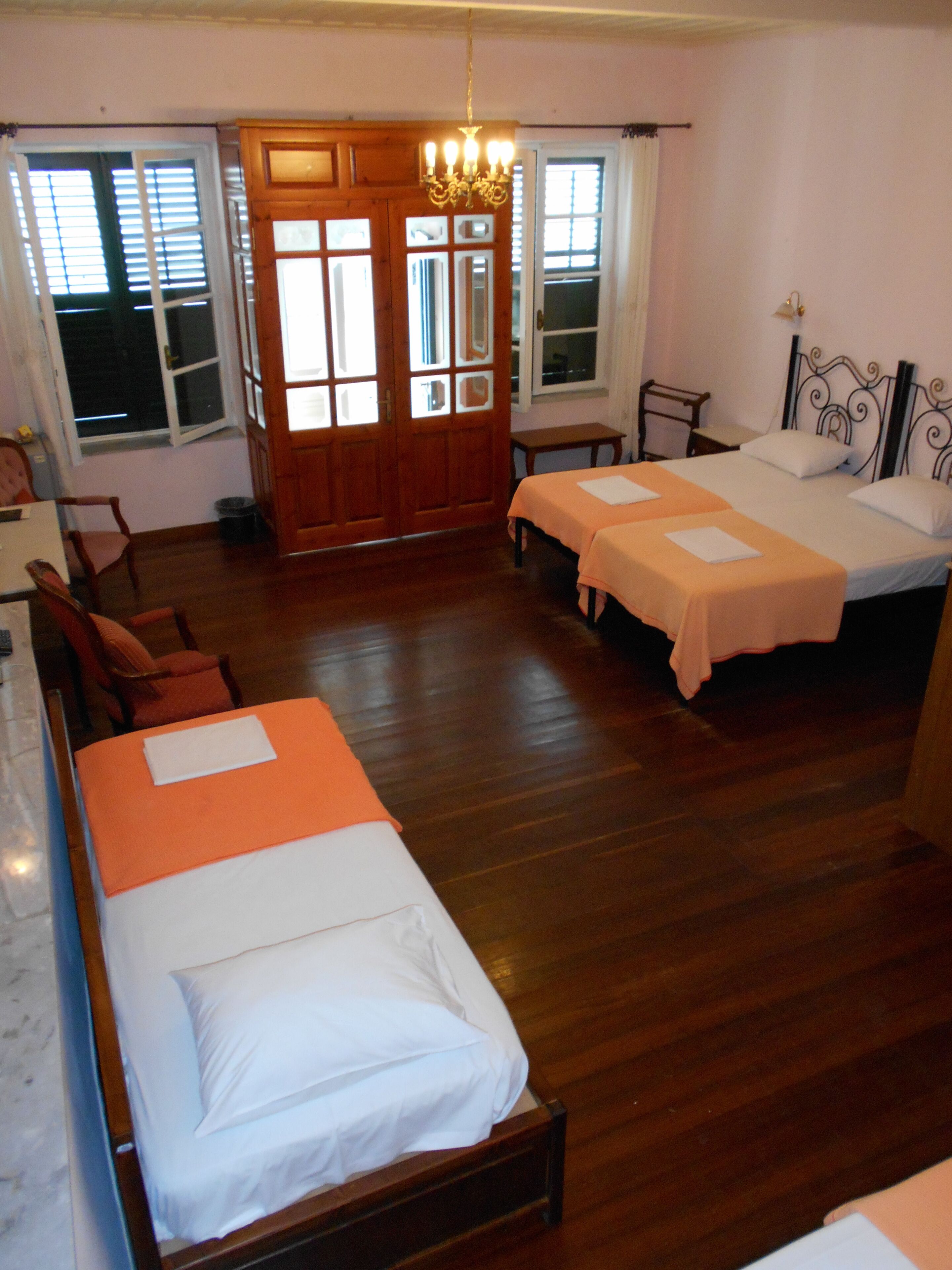 A hotel room with two single beds, a wooden floor, a chandelier, and a window with blinds.