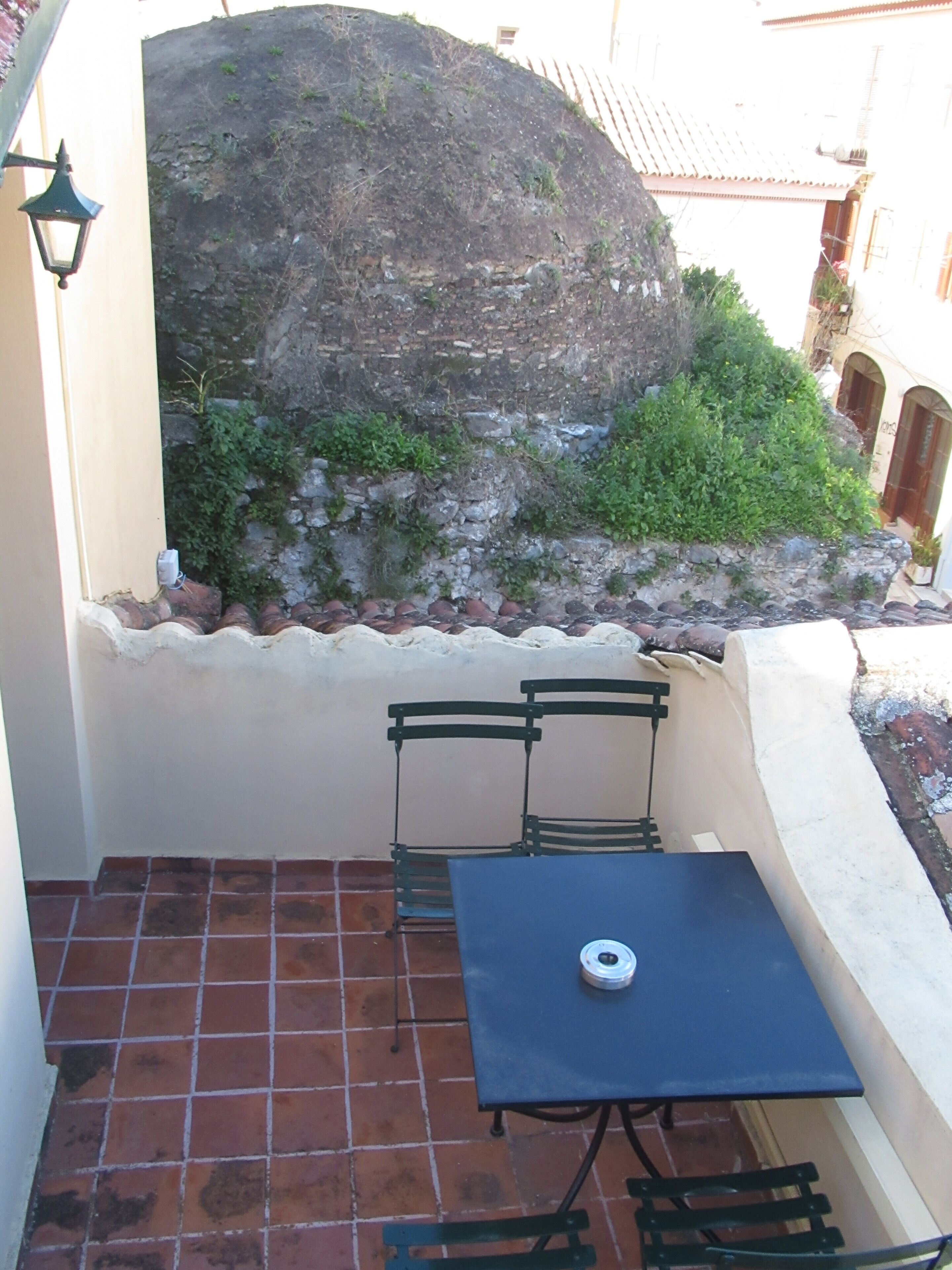 A small outdoor patio with a table and two chairs, a stone wall, and a large rock.