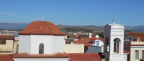 A view of a town with buildings featuring red-tiled roofs and white walls, including a church with a bell tower.