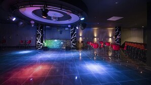 Amplia pista de baile con escenario central, rodeada de sillas rojas y un techo moderno iluminado.