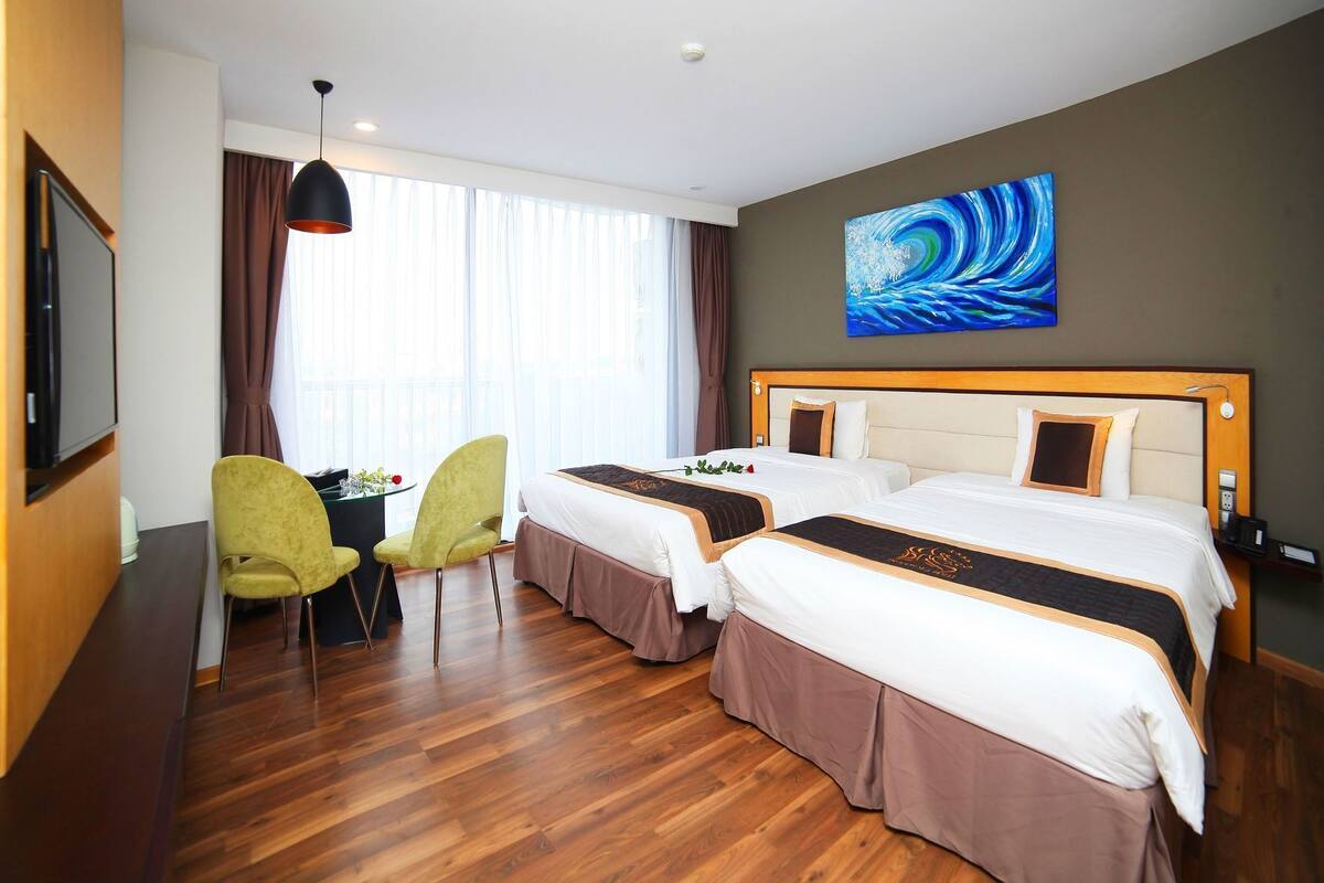 A hotel room with two beds, a desk with a chair, a TV, and a painting on the wall.