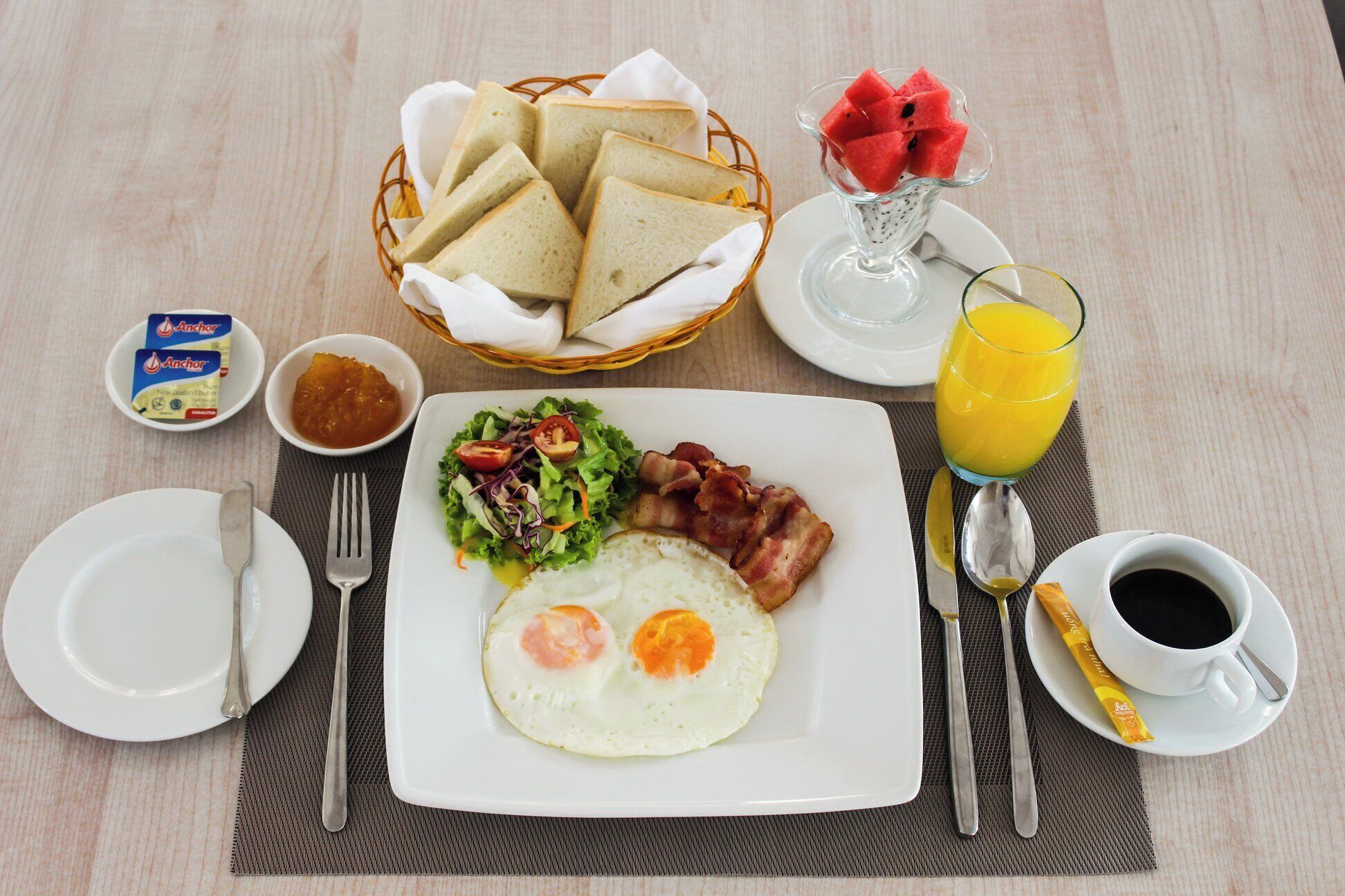 A breakfast setting with toast, eggs, bacon, a salad, and a glass of orange juice.