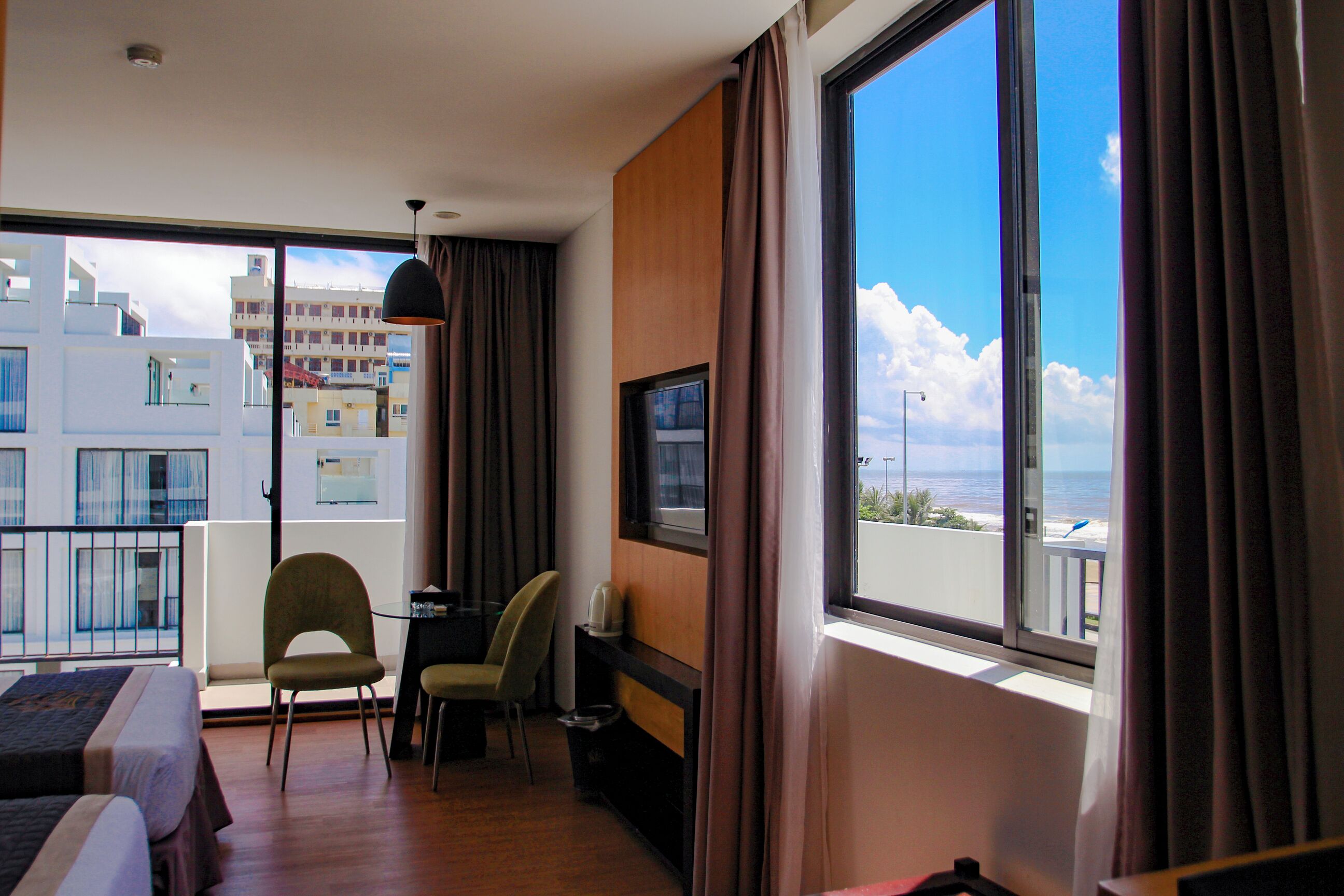 A hotel room with a large window, a bed, two chairs, a desk, and a TV.