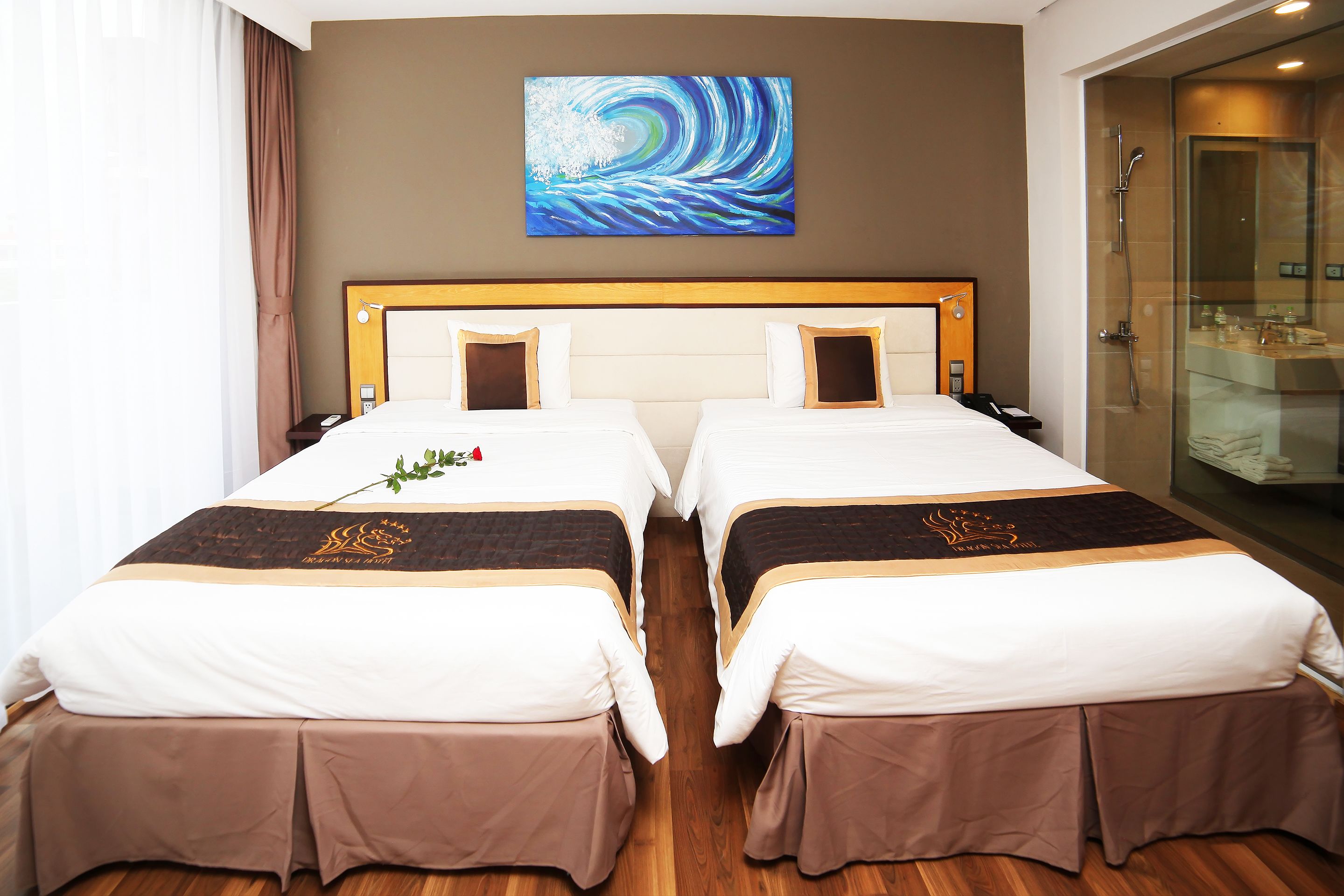 A hotel room with two beds, a large painting on the wall, and a glass shower enclosure.