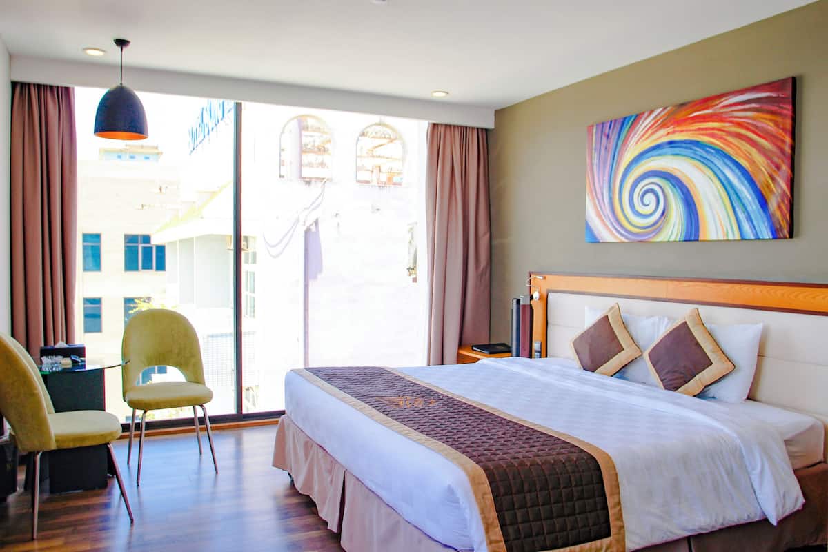 A hotel room with a bed, a chair, a desk, and a large window.