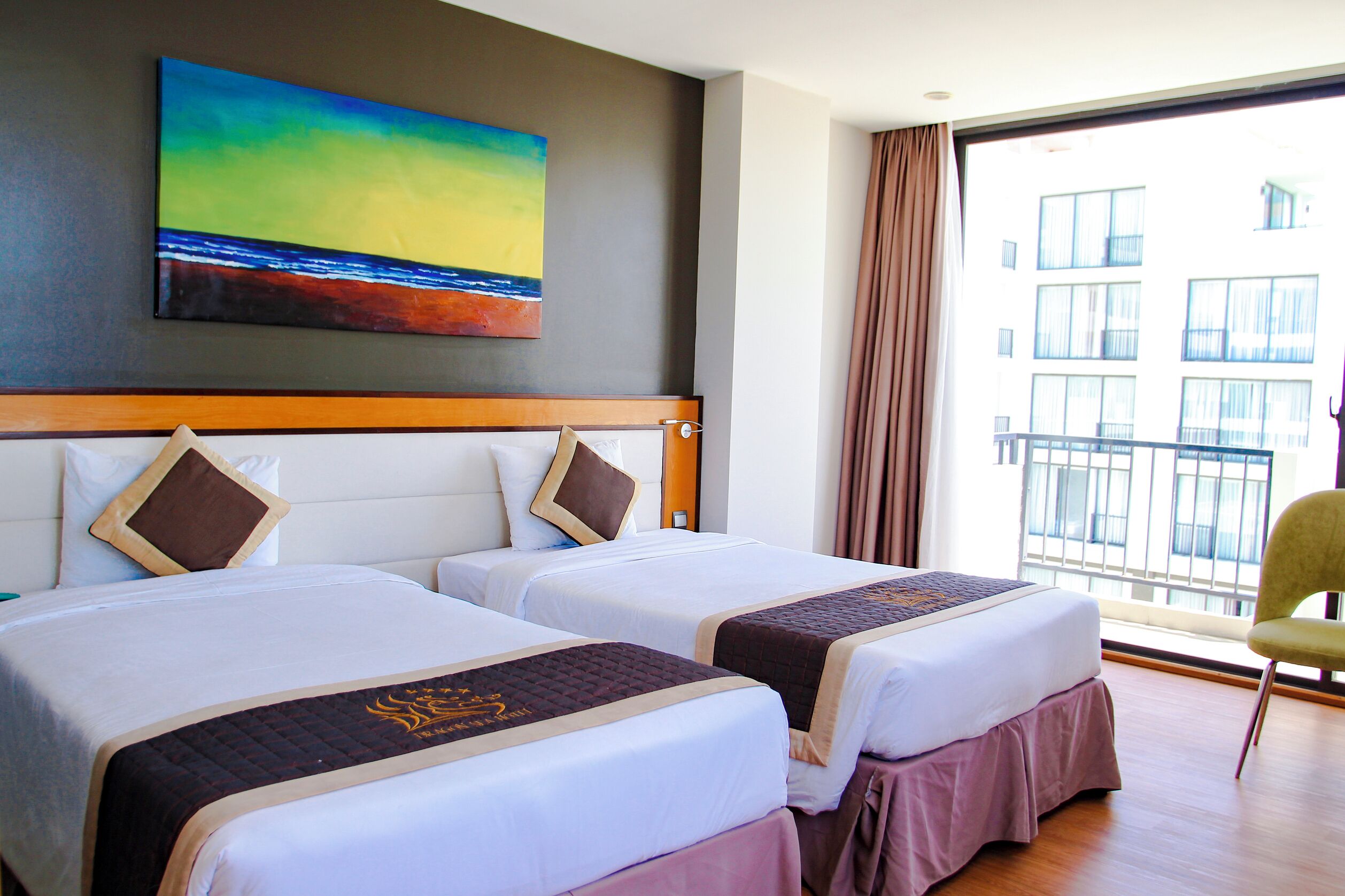 Ein Hotelzimmer mit zwei Betten, einem Bild an der Wand und Blick auf ein Gebäude durch ein Fenster.