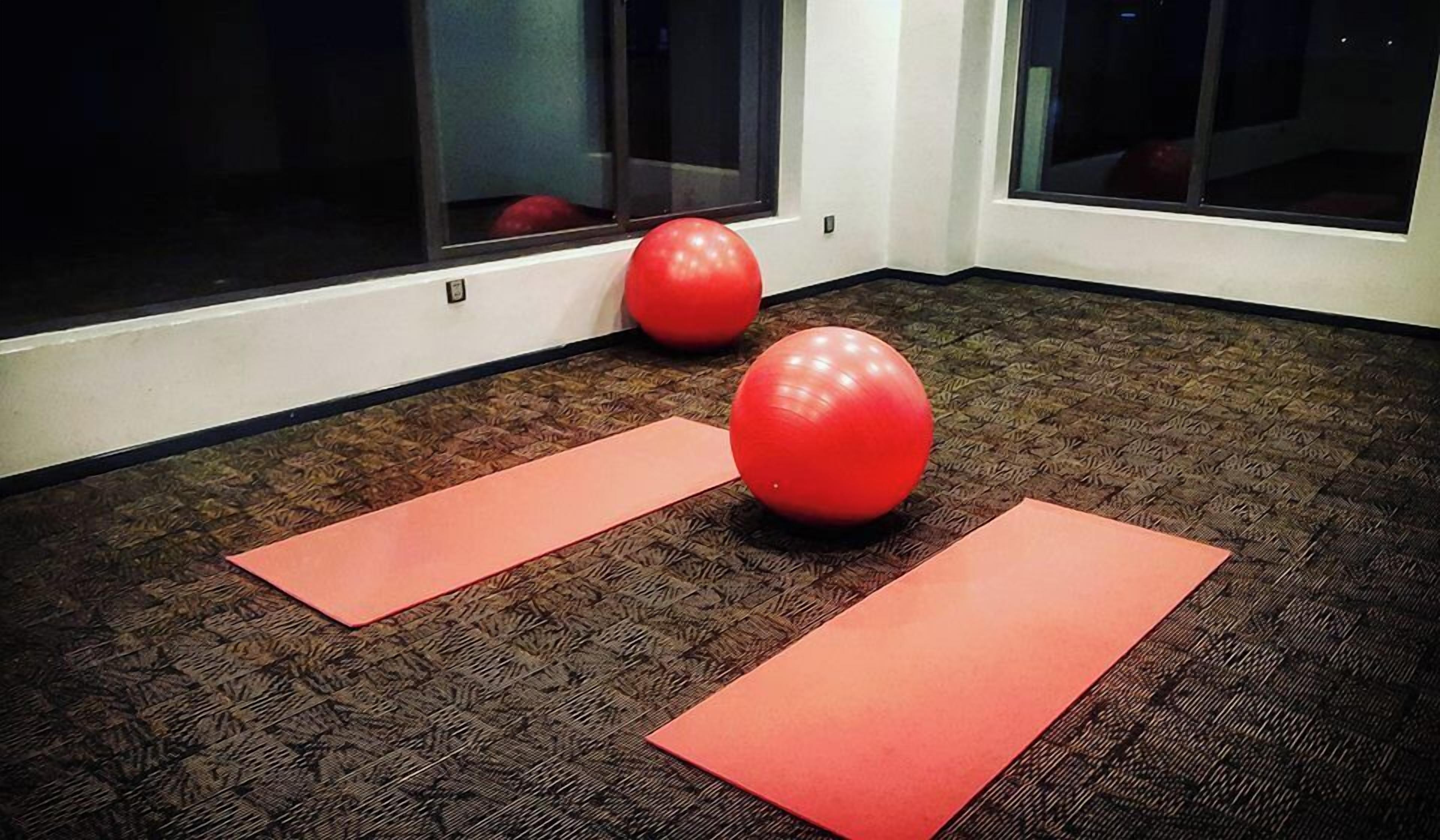 Ein Zimmer mit gemustertem Teppich, zwei roten Gymnastikbällen und zwei roten Übungsmatten.