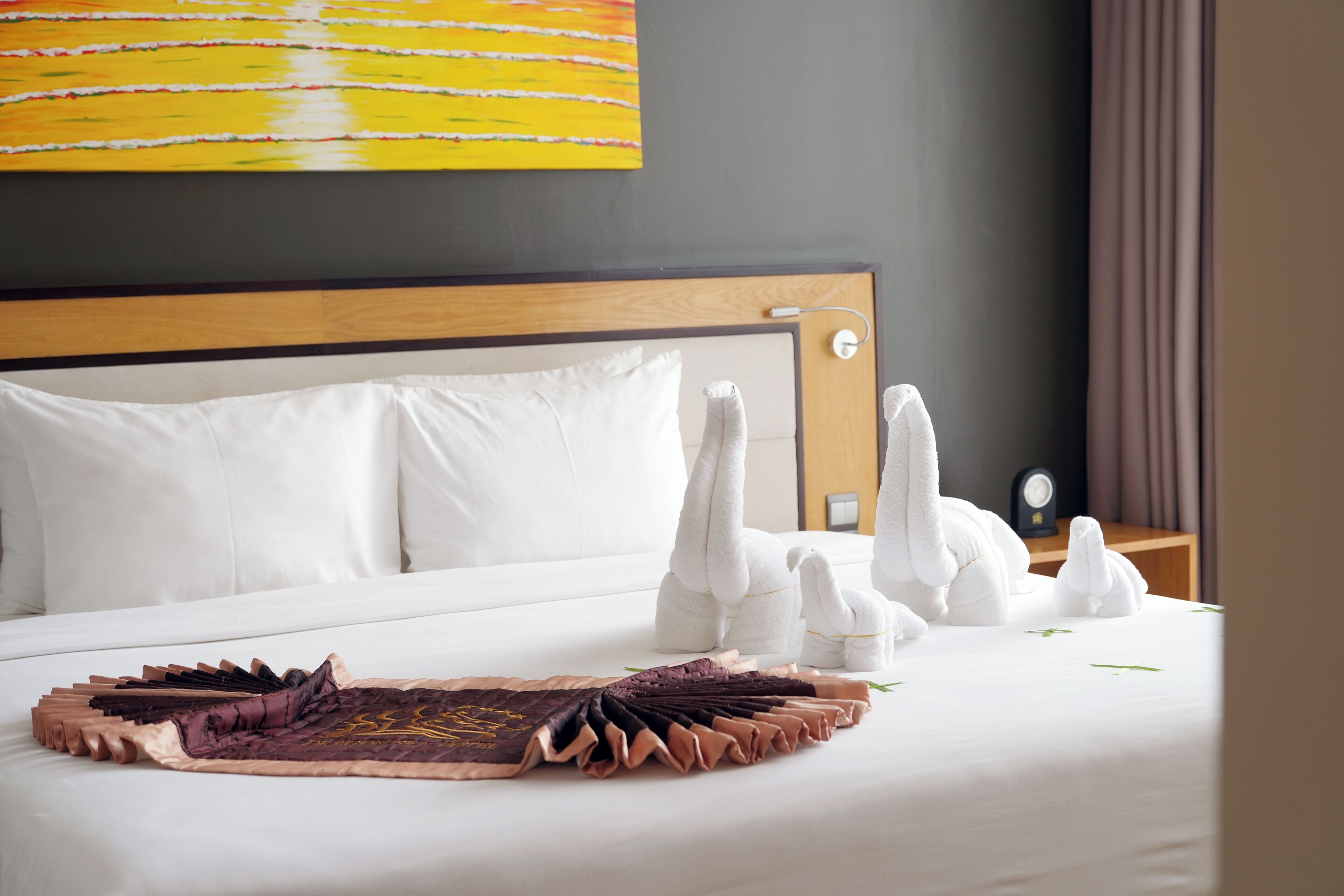 A neatly made bed with white pillows, a decorative headboard, and a wall painting.