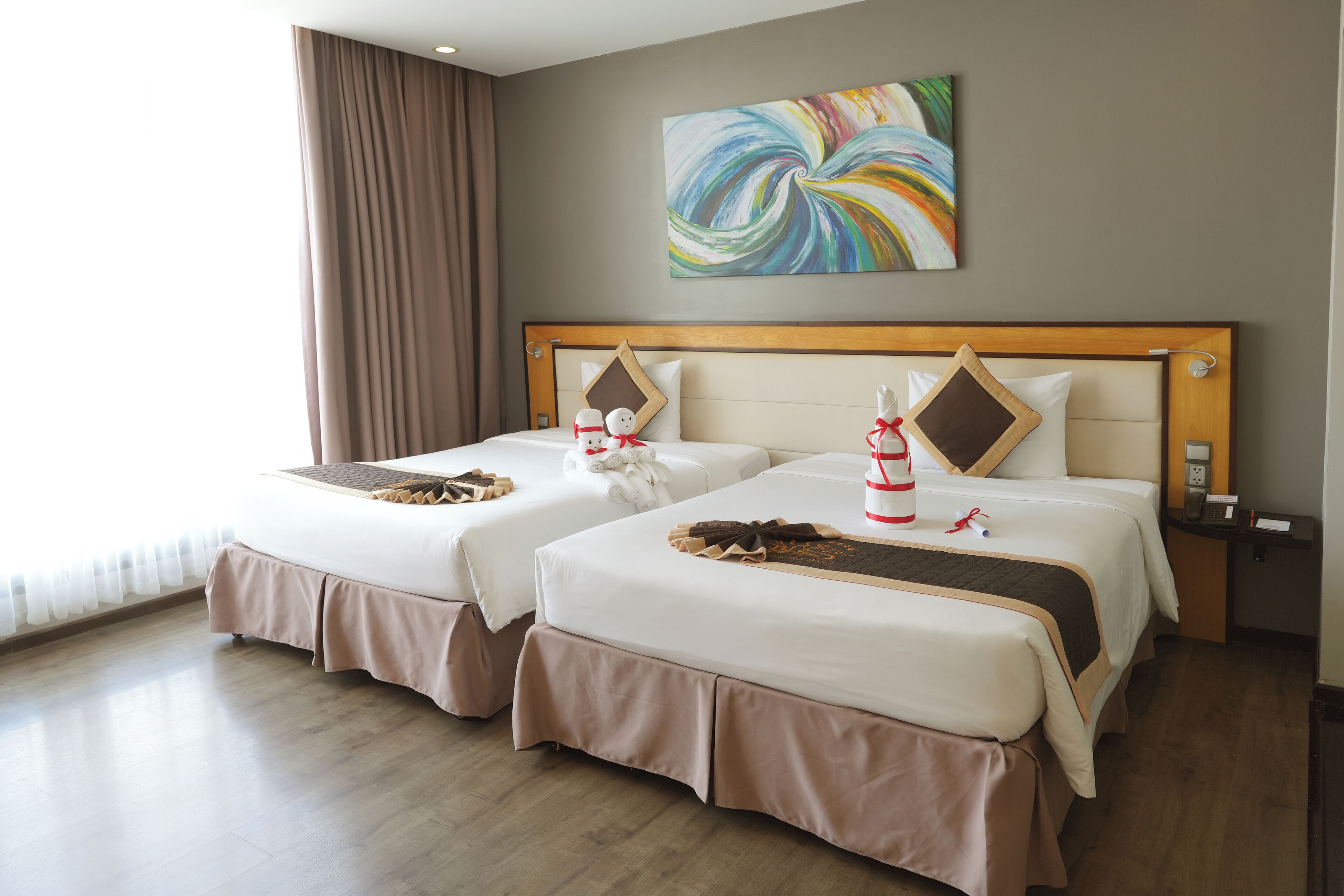 A hotel room with two beds, a wooden headboard, a colorful abstract painting, and a nightstand with a phone.