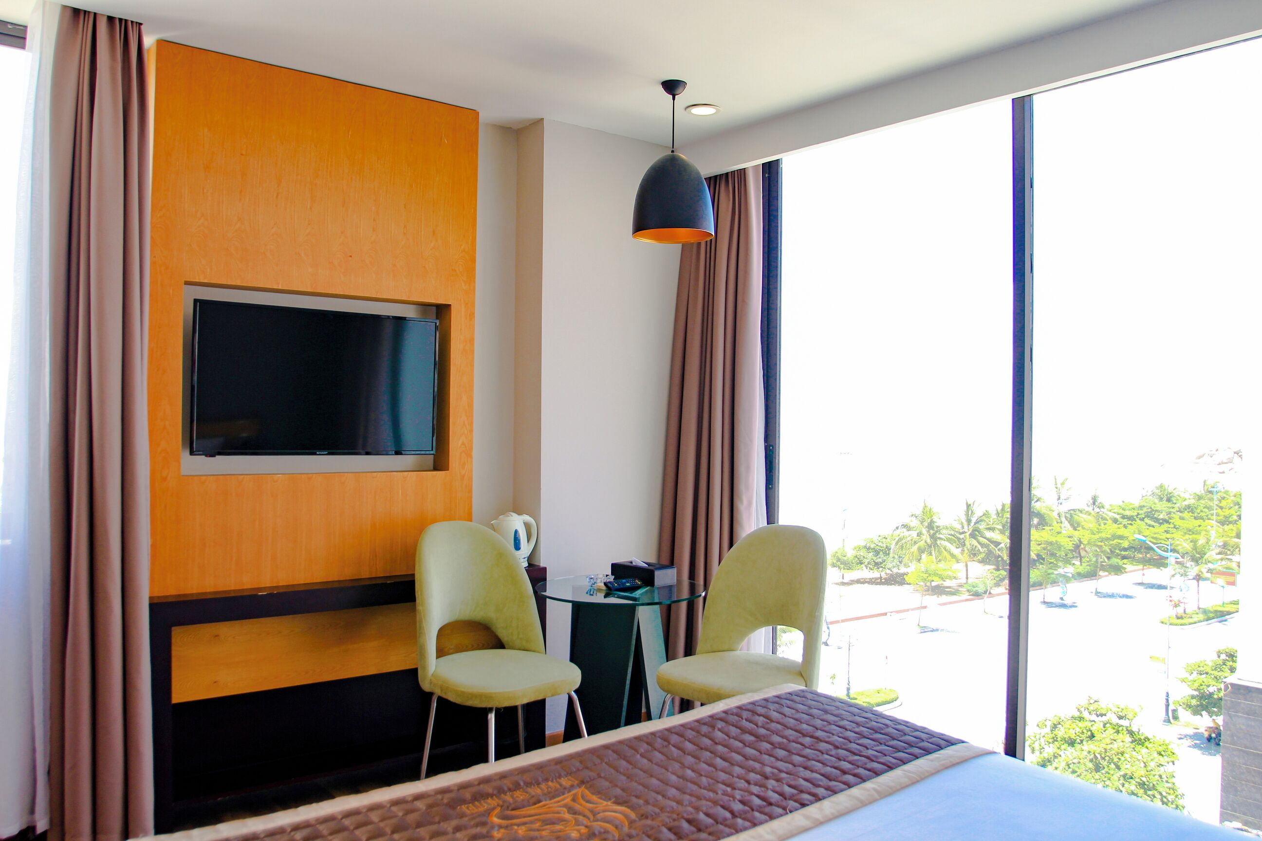 Une chambre d’hôtel avec un lit, deux chaises, un téléviseur fixé au mur et une vue sur l’extérieur.