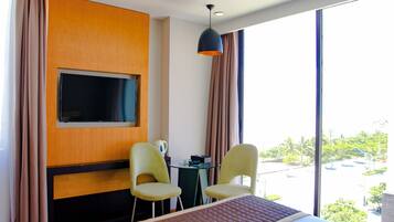 Une chambre d’hôtel avec un lit, deux chaises, un téléviseur fixé au mur et une vue sur l’extérieur.