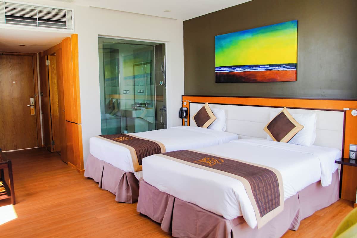 A hotel room with two beds, a glass shower area, a painting on the wall, and a wooden floor.