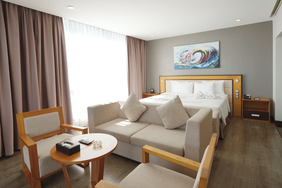 A hotel room with a bed, a sofa, a table, and a painting on the wall.