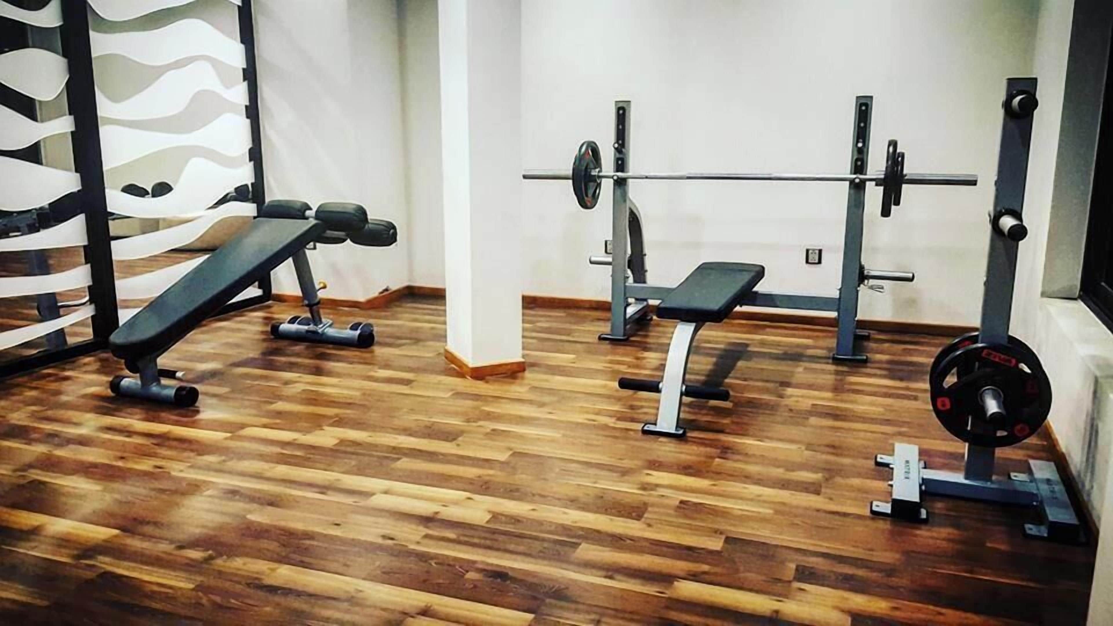 A gym with wooden flooring, weightlifting equipment, and benches.