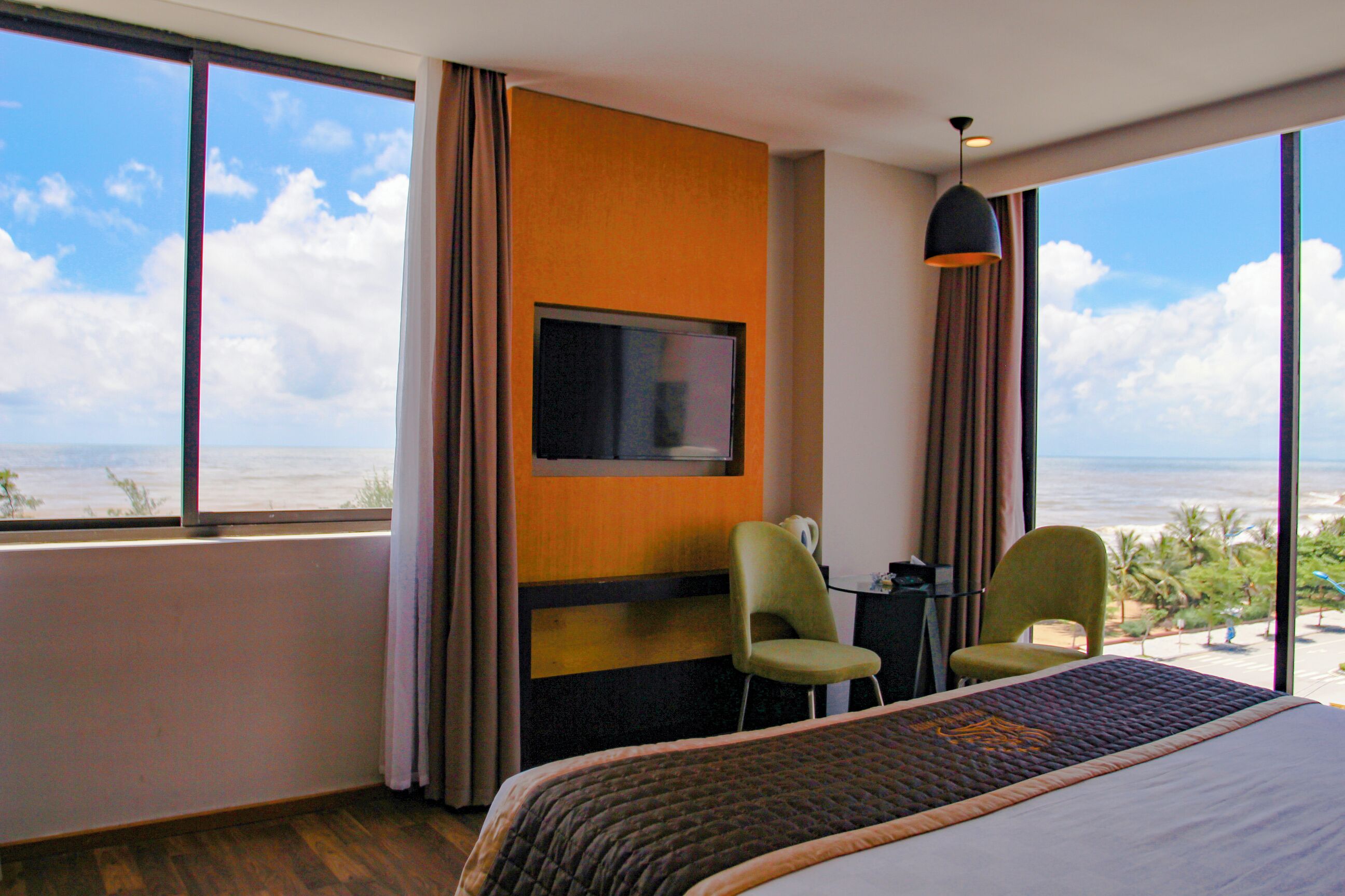 A hotel room with a bed, two chairs, a TV, and a view of the ocean.