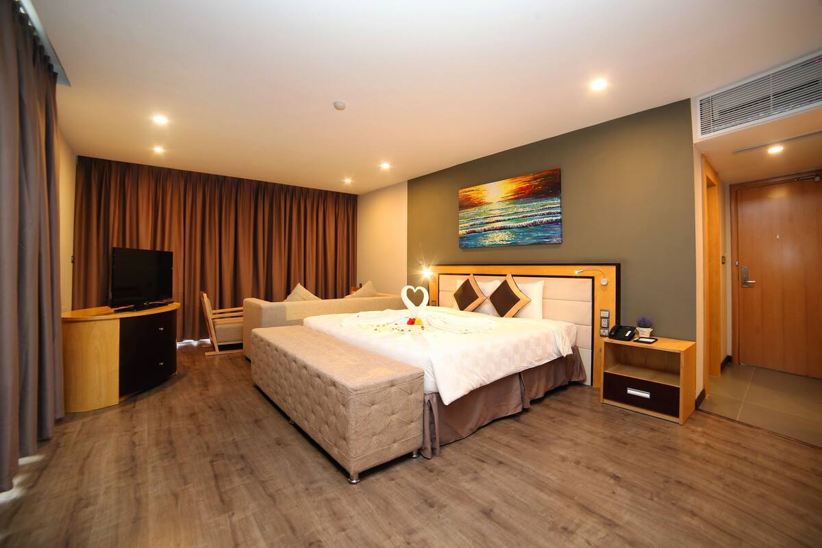 A hotel room with a large bed, a TV, a desk, a chair, and a painting on the wall.