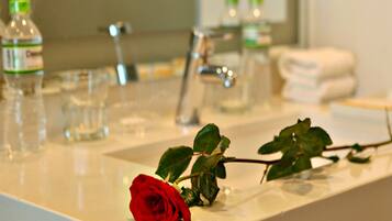 Un lavandino in bagno con una rosa rossa, flaconi, bicchieri e asciugamani.