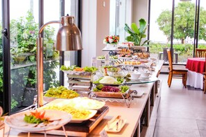 A buffet with various food items and a large window with a view of greenery. - Dragon Sea Sam Son Hotel (Sam Son)
