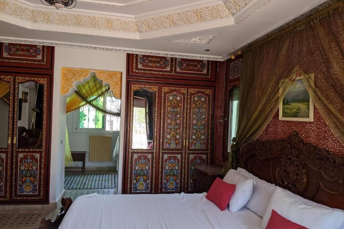 Una habitación con una cama grande, paneles de madera ornamentados y vistas a otra estancia.
