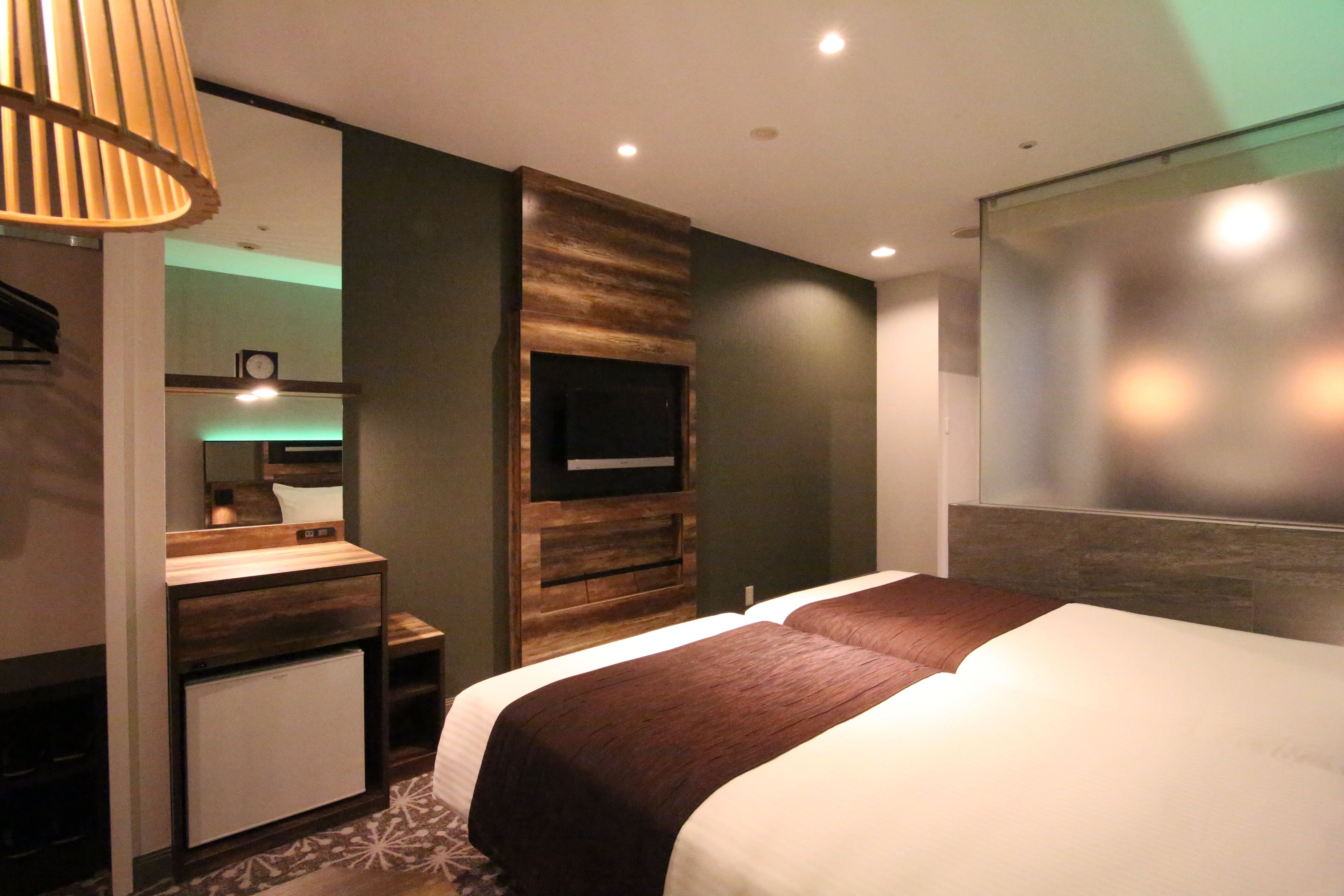 Une chambre d’hôtel moderne avec un grand lit, un téléviseur intégré, une petite kitchenette et un miroir.