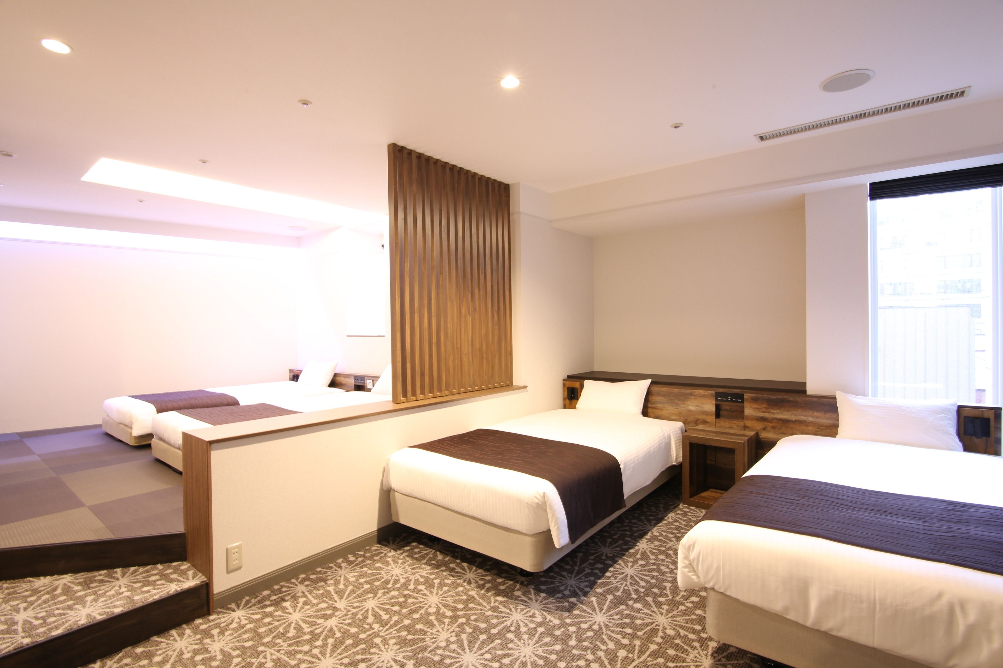 A hotel room with two beds, a wooden headboard, a large window, and a patterned carpet.