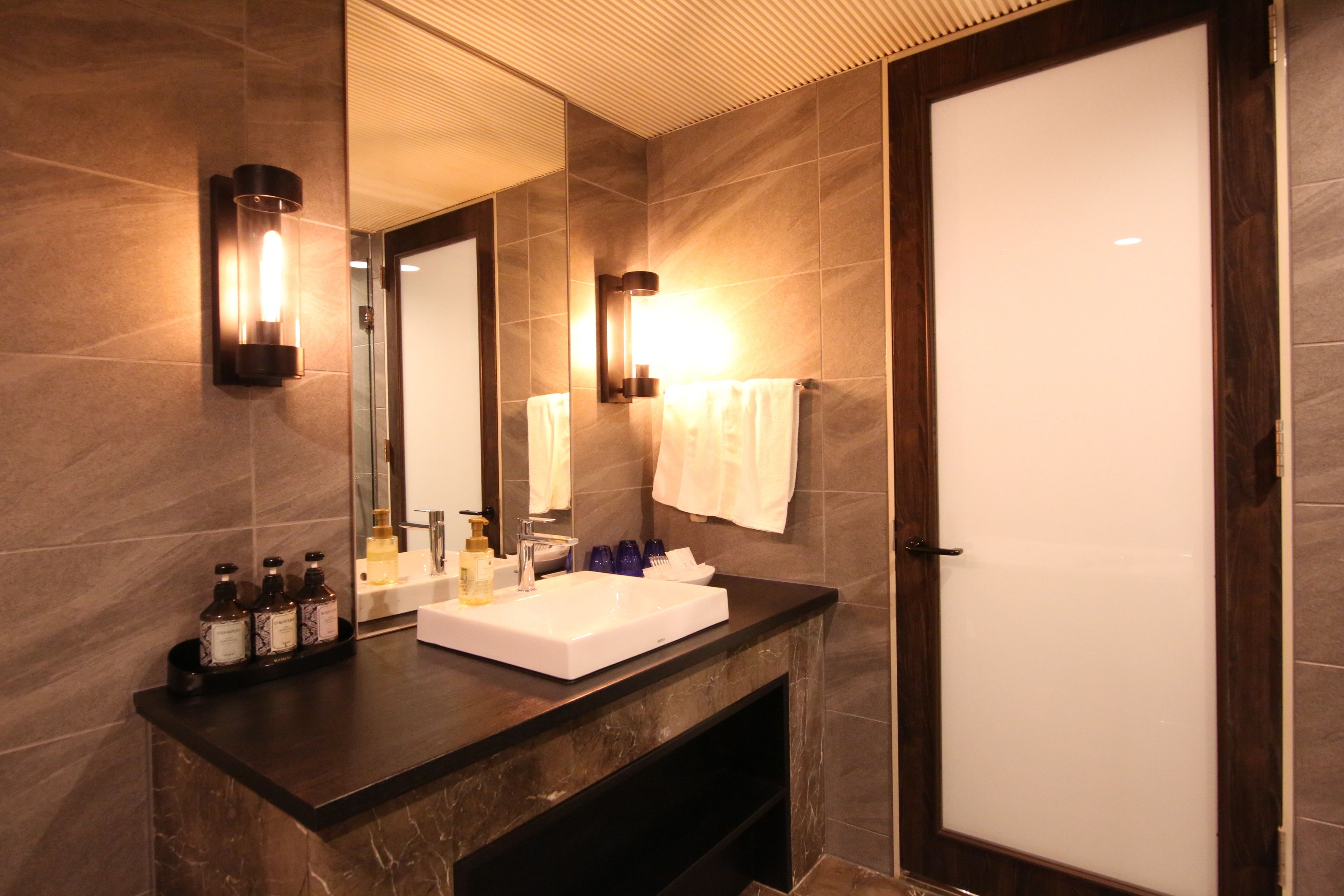 A modern bathroom with a large mirror, a white sink, and two wall-mounted lights.