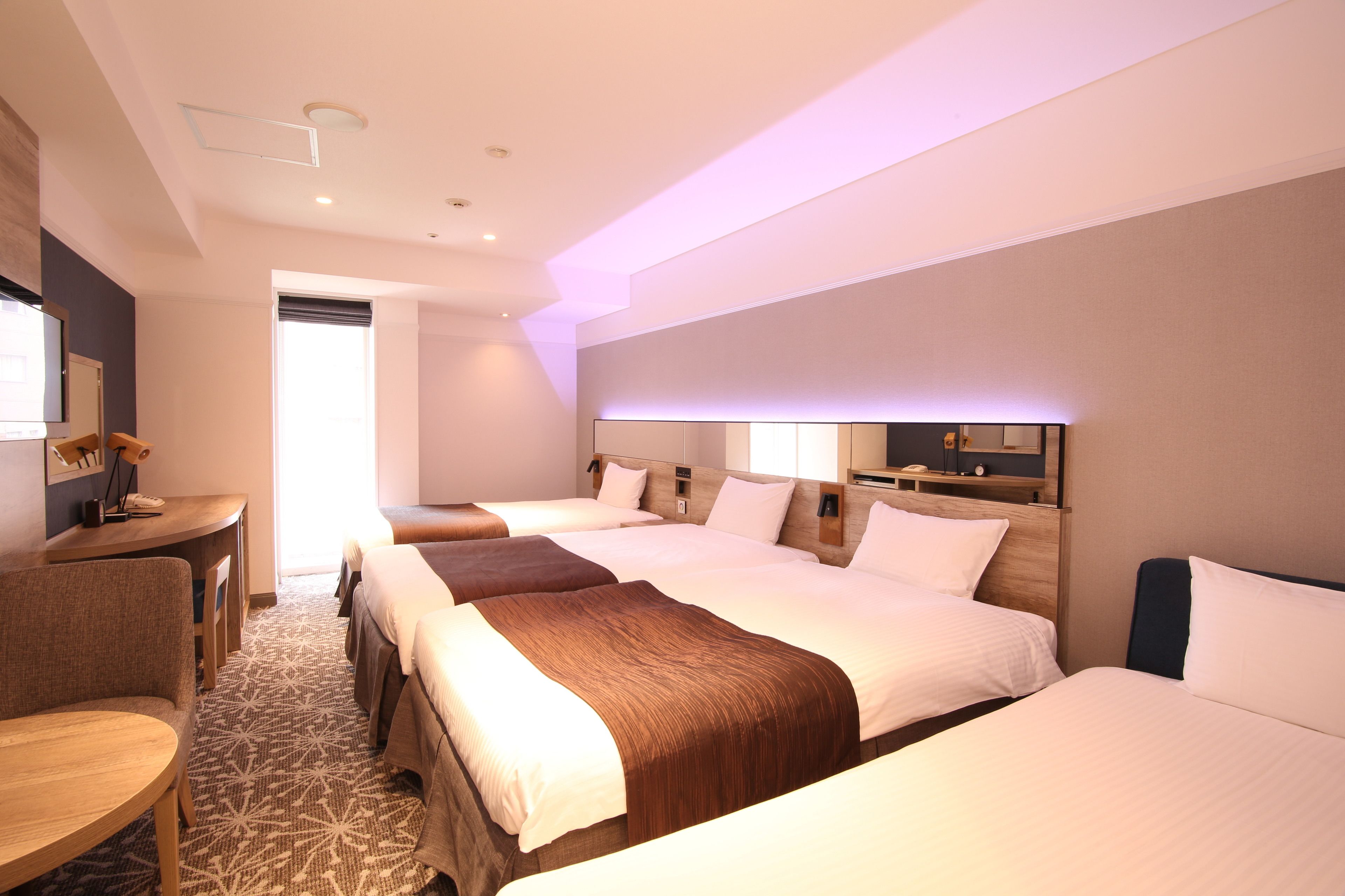 A hotel room with three beds, a desk, and a chair.