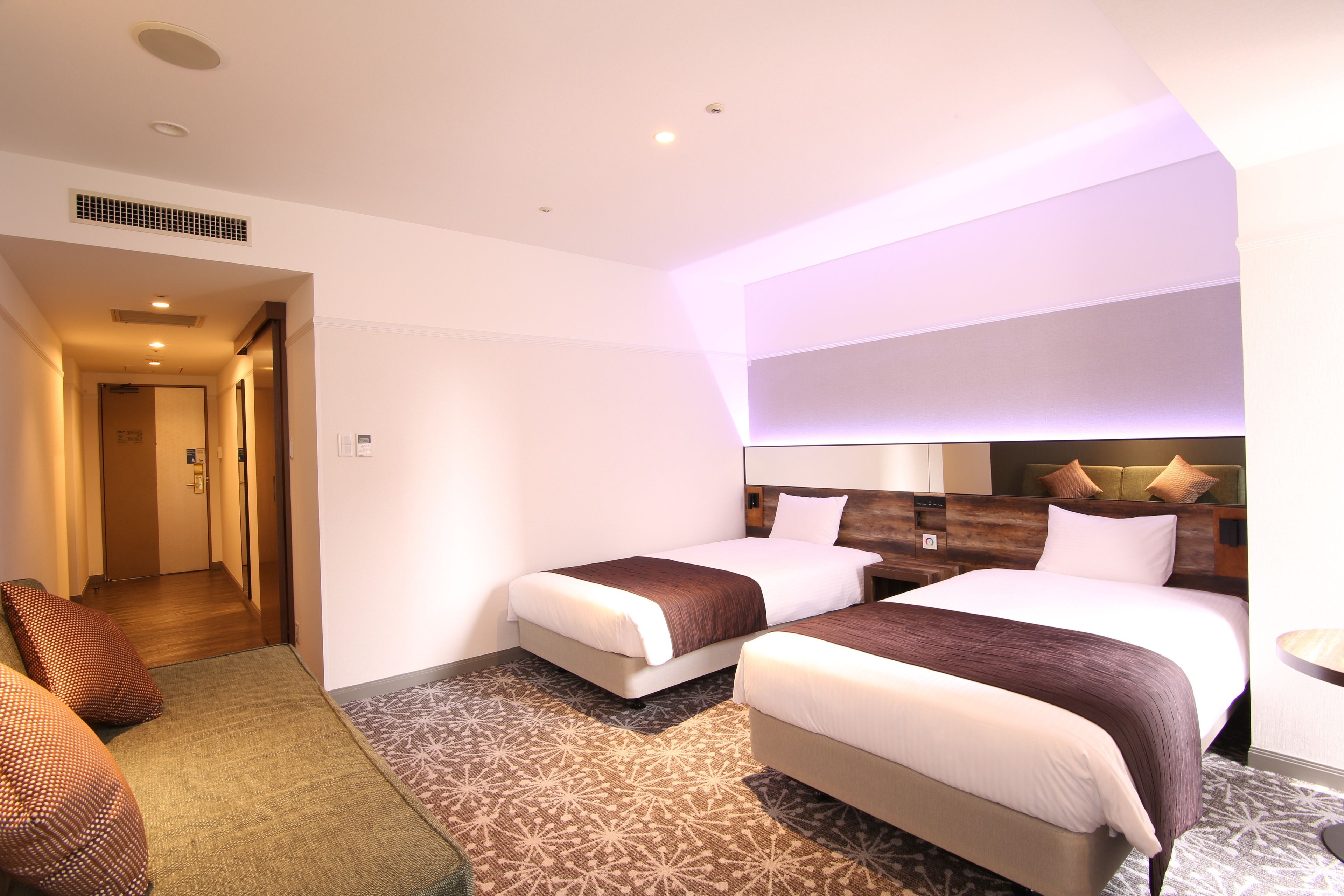 Habitación de hotel con dos camas, un área de descanso con sofá y una mesita.