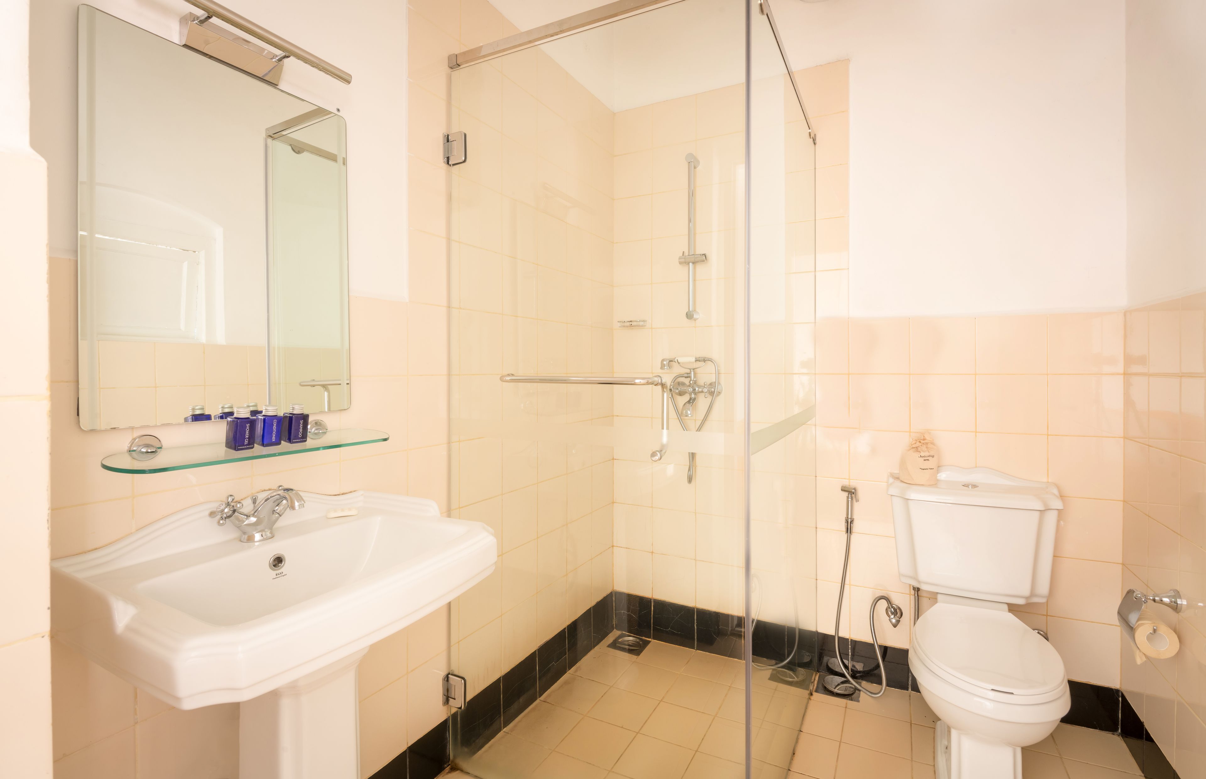 A bathroom with a sink, mirror, glass shower enclosure, toilet, and tiled walls.