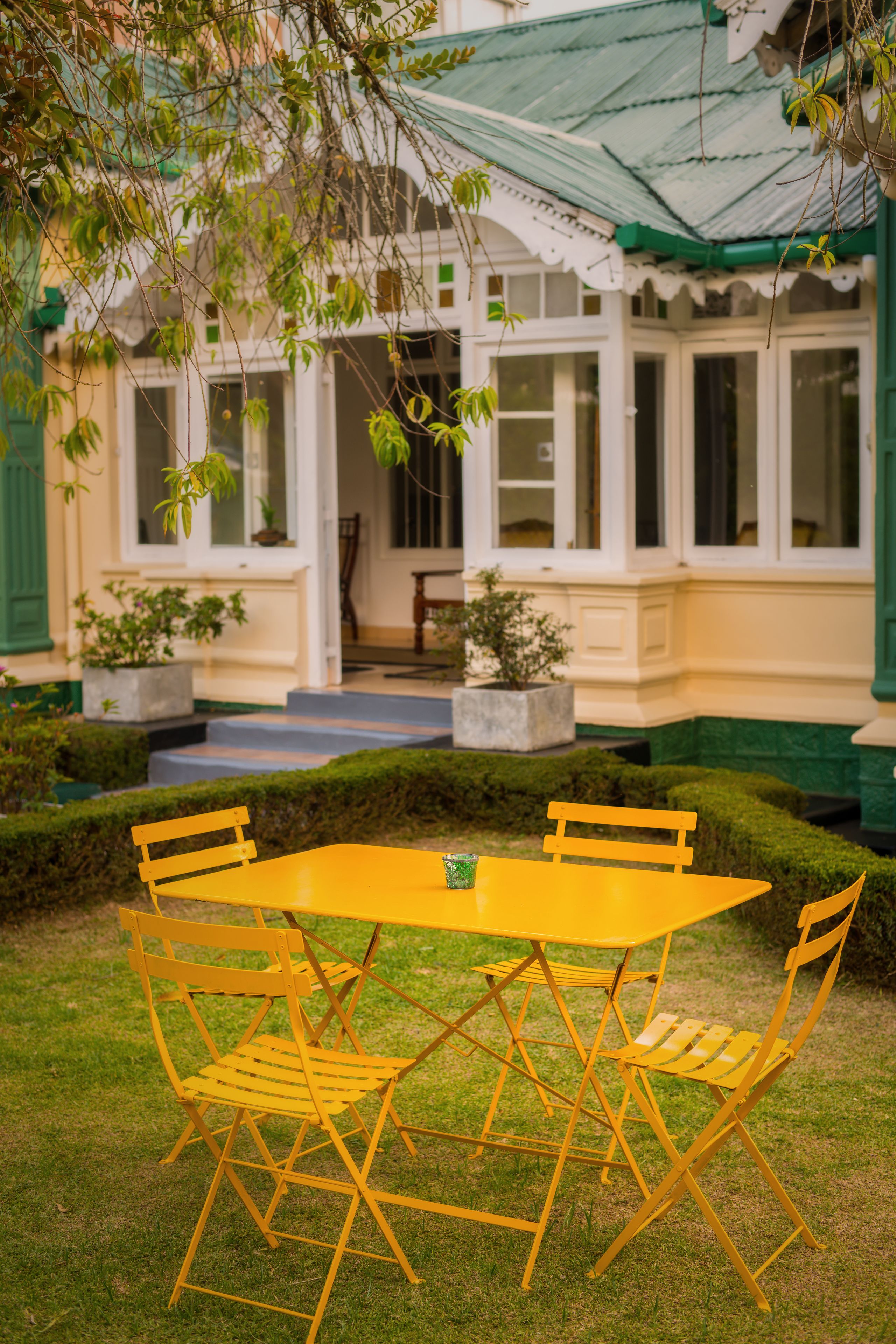 A yellow table and chairs set in a garden area with a building in the background.