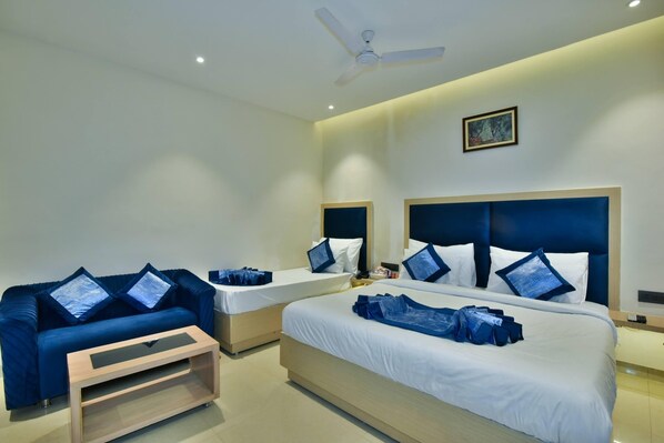 A hotel room with two beds, a sofa, a ceiling fan, and a painting on the wall. - Hotel Puri Palace Amritsar (Amritsar)