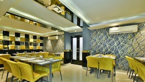 Un restaurante moderno con sillas y mesas amarillas, diseños geométricos en las paredes y una escalera que lleva a un nivel superior.