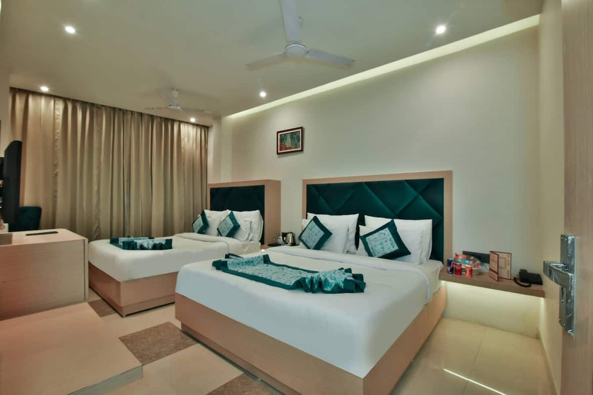 A hotel room with two beds, a desk, a chair, a ceiling fan, and a small table with items on it.