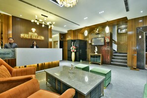 A hotel reception area with a wooden reception desk, a flat-screen TV, and a staircase leading to the upper floor. - Hotel Puri Palace Amritsar (Amritsar)