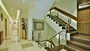 Un hall de hotel con una escalera central, una recepción y un jarrón decorativo con flores.