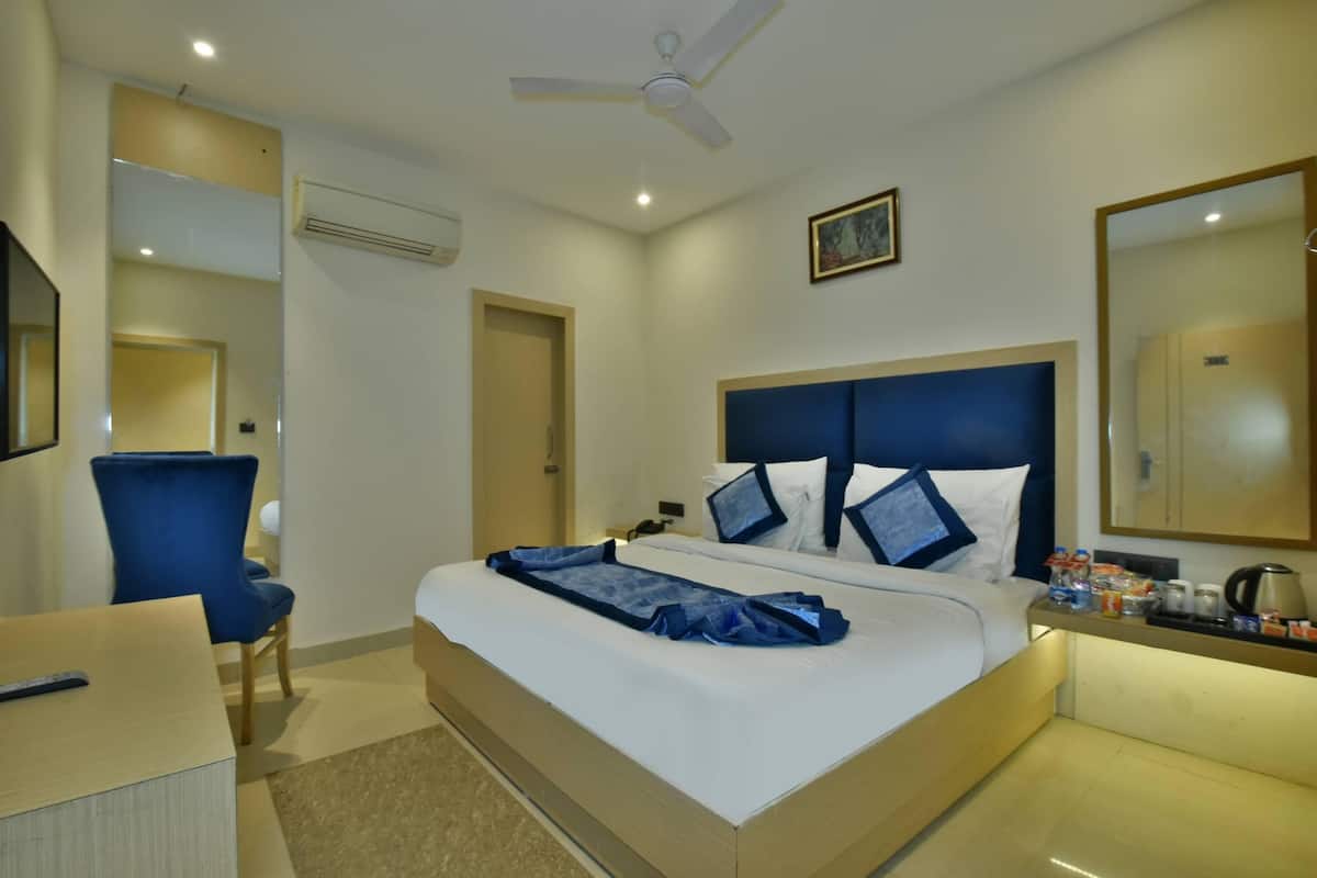 A hotel room with a bed, a chair, a desk, a ceiling fan, and a nightstand with a lamp and a coffee maker.
