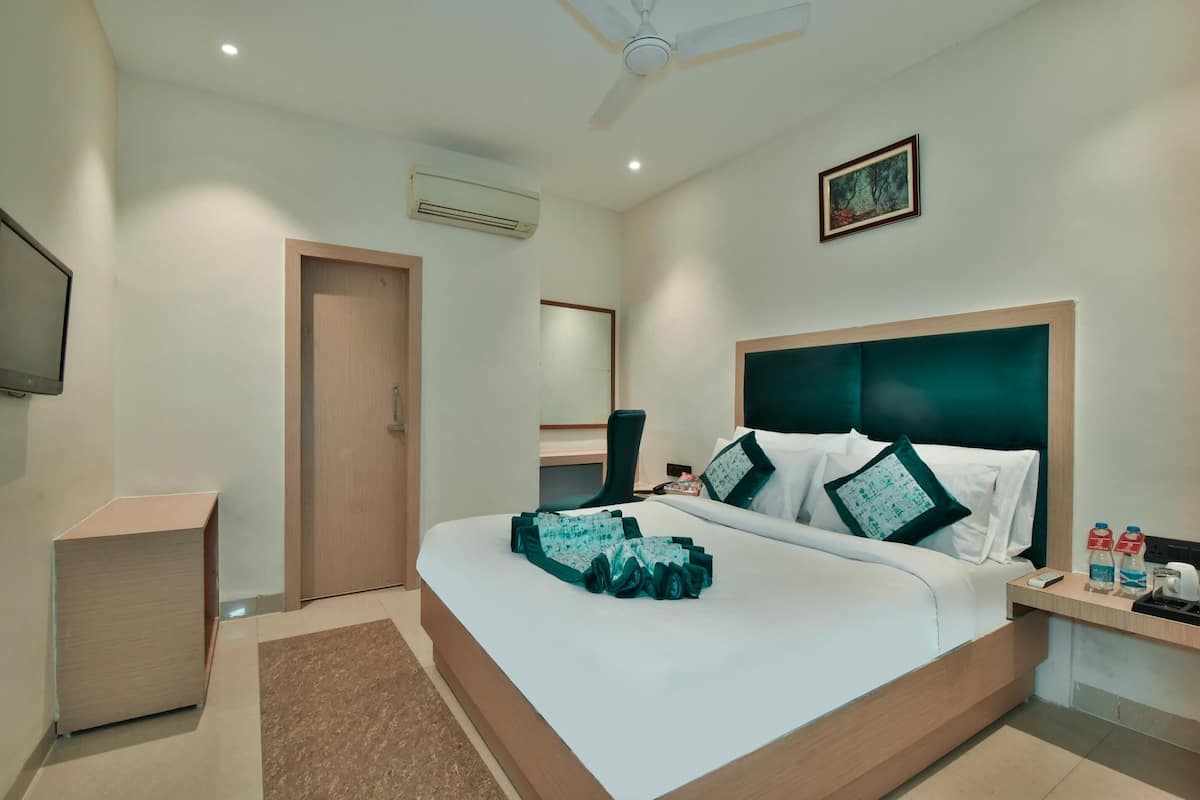 A hotel room with a bed, bedside table, air conditioning unit, ceiling fan, and a painting on the wall.