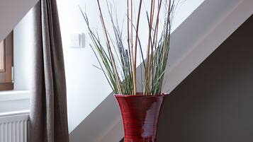 Un florero rojo con plantas verdes sobre un suelo de madera cerca de una ventana con cortinas.