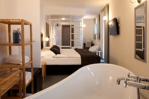 A modern hotel room with a large bathtub, wooden shelves with towels, a neatly made bed, and a television mounted on the wall. - Hotel Koruna (Chlumec nad Cidlinou)