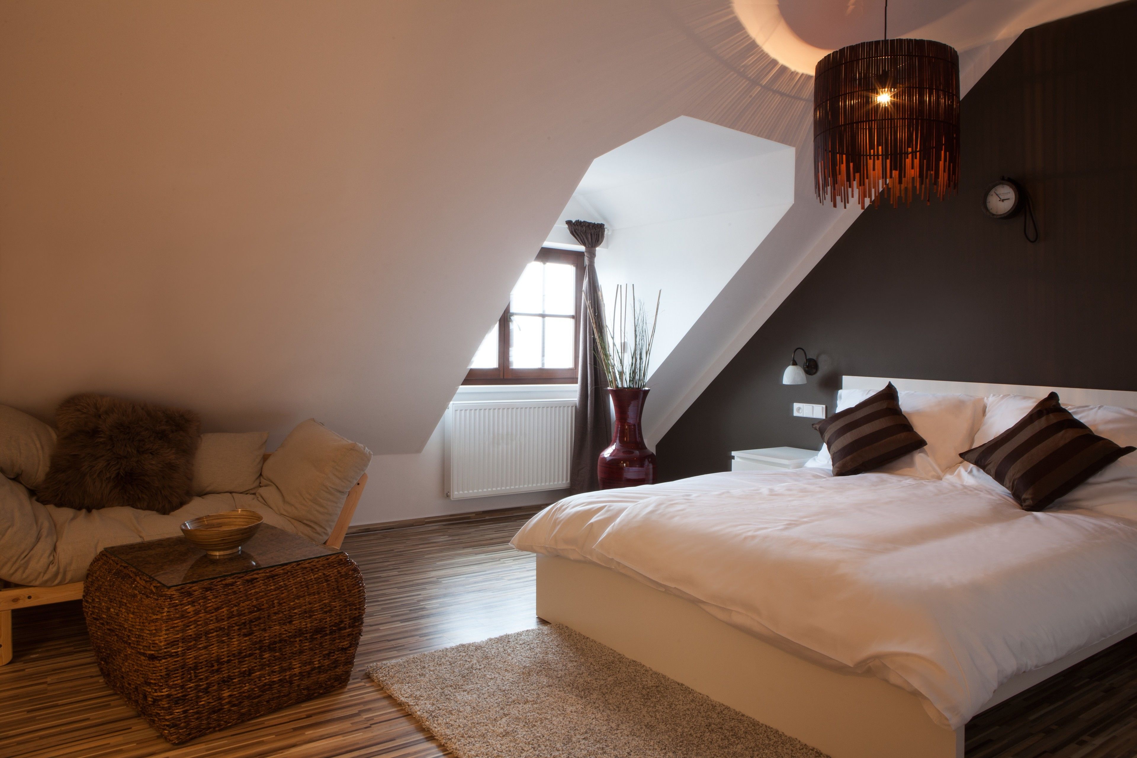Ein Schlafzimmer mit einem großen Bett, einer Hängelampe, einer Vase und Blick ins Freie.