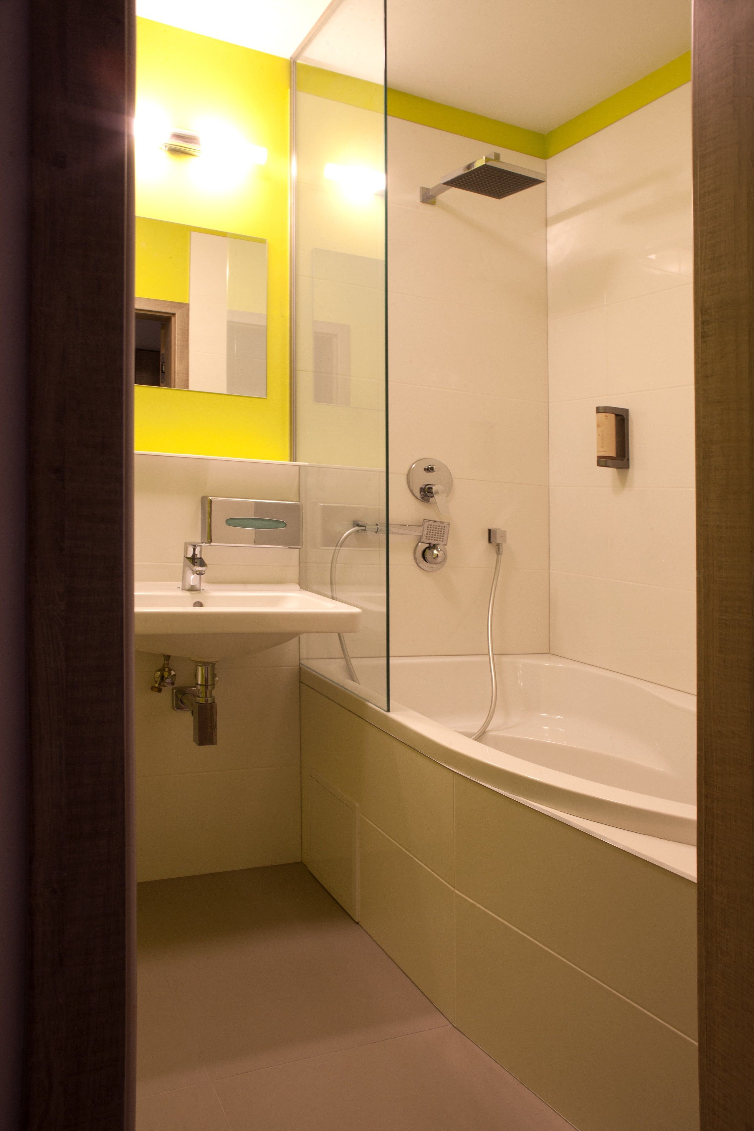 A modern bathroom with a white sink, a glass-enclosed shower, and a yellow accent wall.