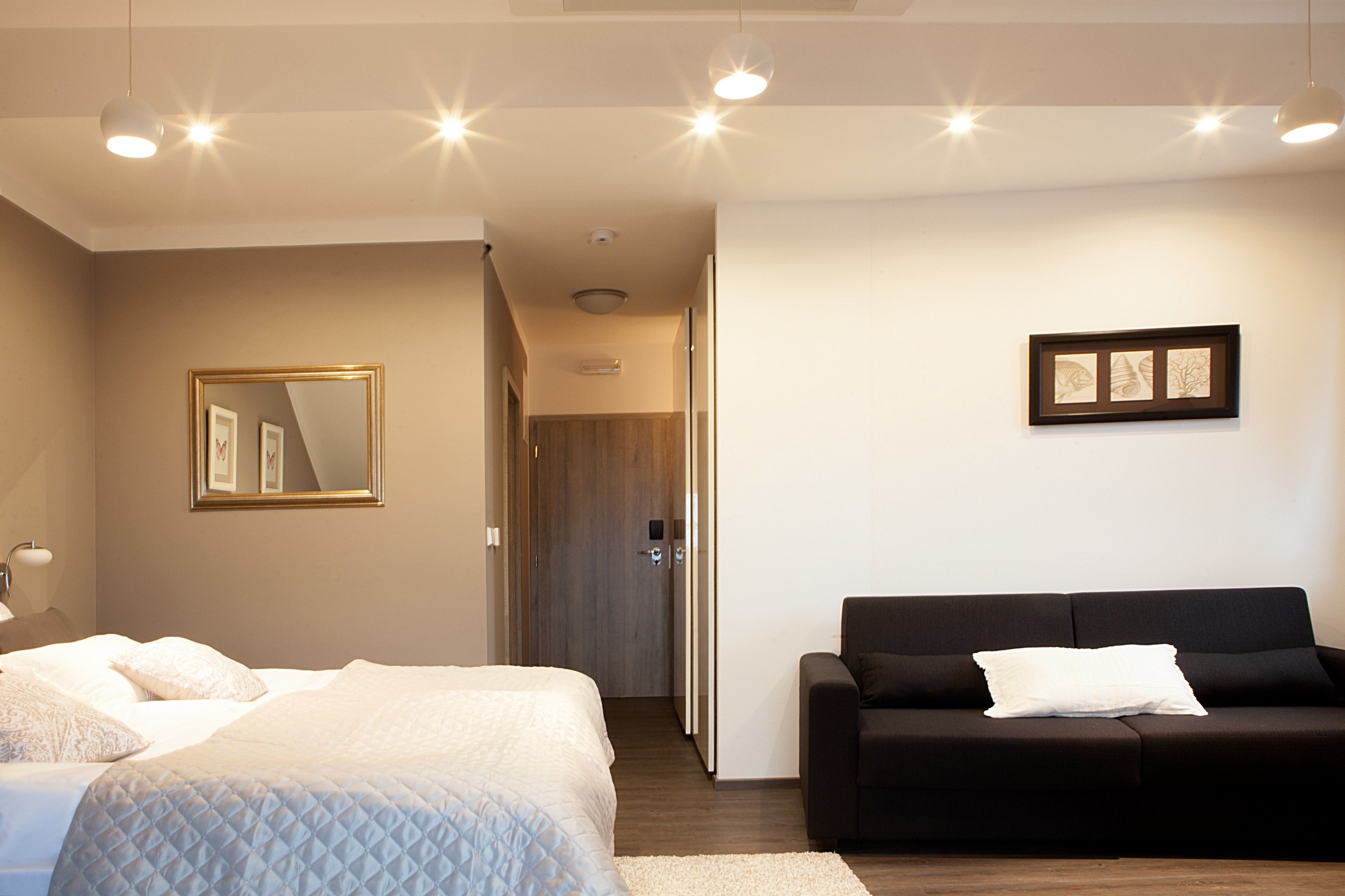 Una habitación de hotel con una cama, un sofá negro, un cuadro enmarcado en la pared y una puerta que da a otra habitación.