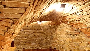Un interior de paredes de piedra con bancos de madera y suelo de baldosas.