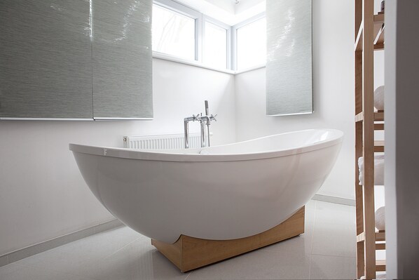 Een moderne badkamer met een vrijstaand bad, grote ramen en een houten vloer.