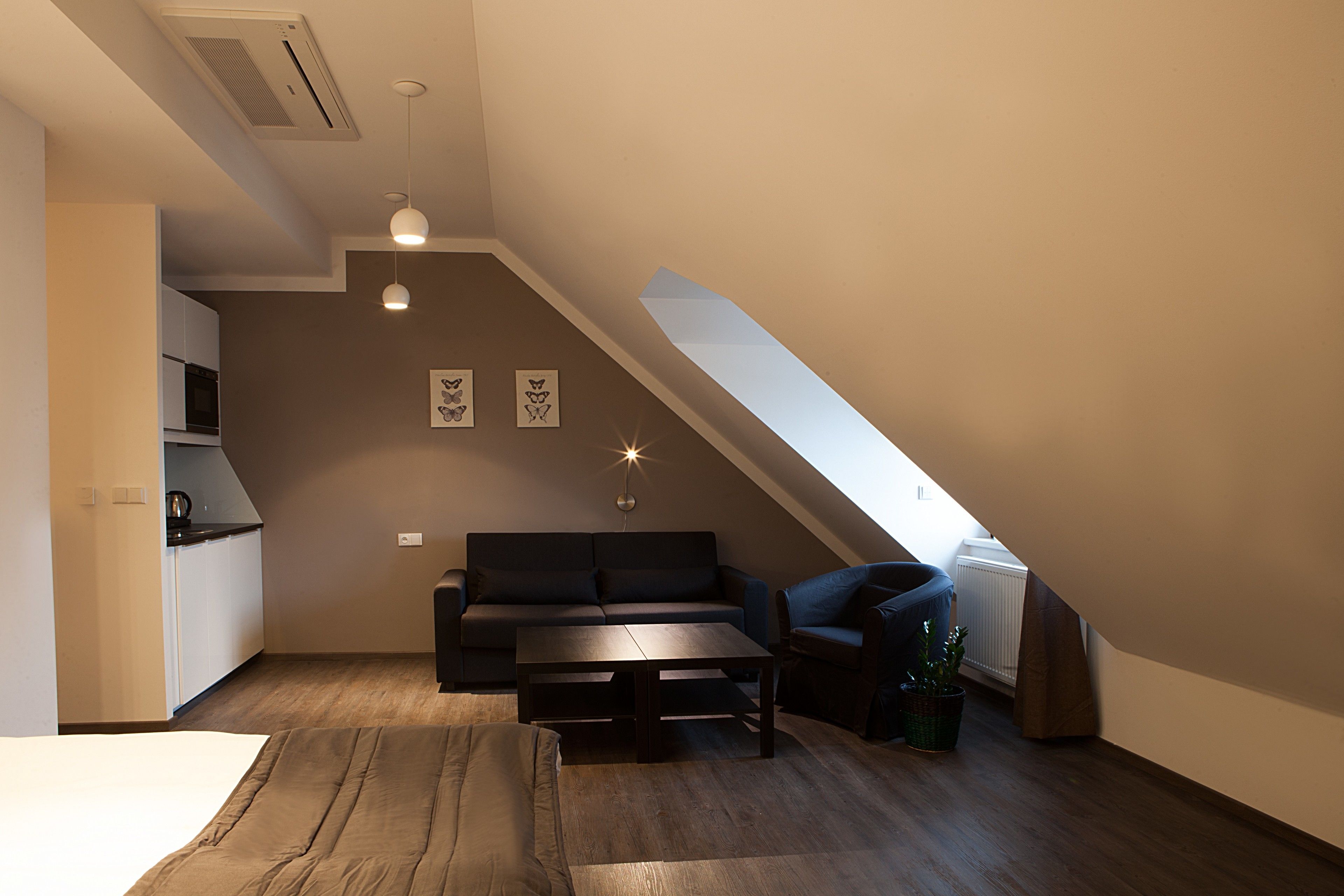 Un dormitorio tipo loft moderno con techo inclinado, un sofá oscuro, una mesita pequeña y una planta en maceta.
