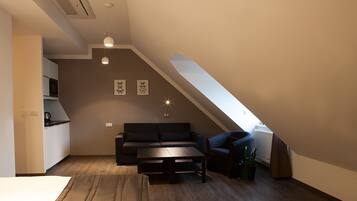 Un dormitorio tipo loft moderno con techo inclinado, un sofá oscuro, una mesita pequeña y una planta en maceta.