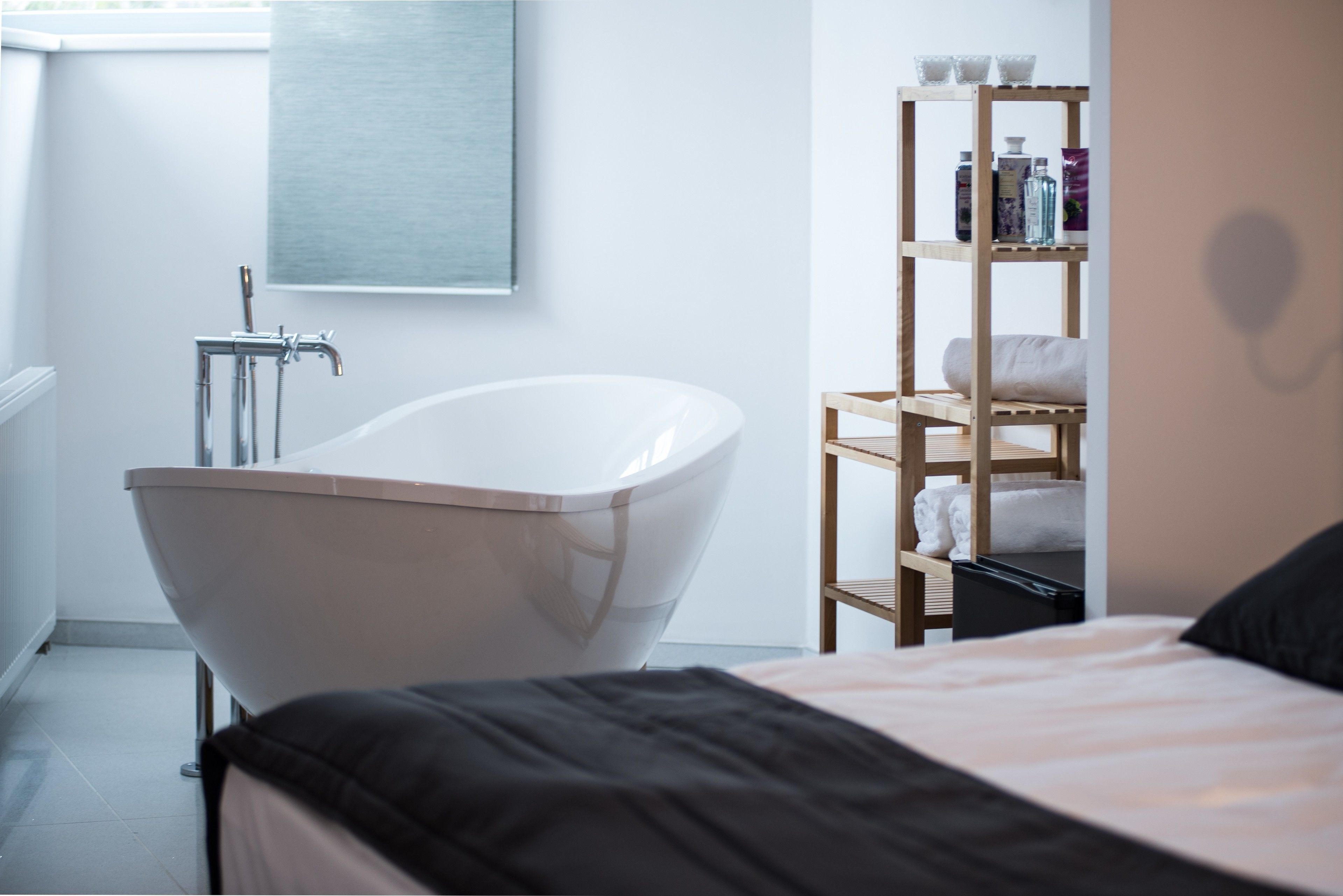 Un baño moderno con una bañera independiente, un estante de madera con artículos de aseo y un ventanal grande.